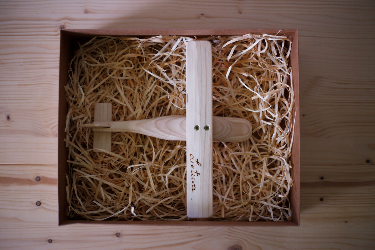 A small wooden airplane model presented inside a brown gift box filled with shredded paper, photographed from above on a light wood surface.